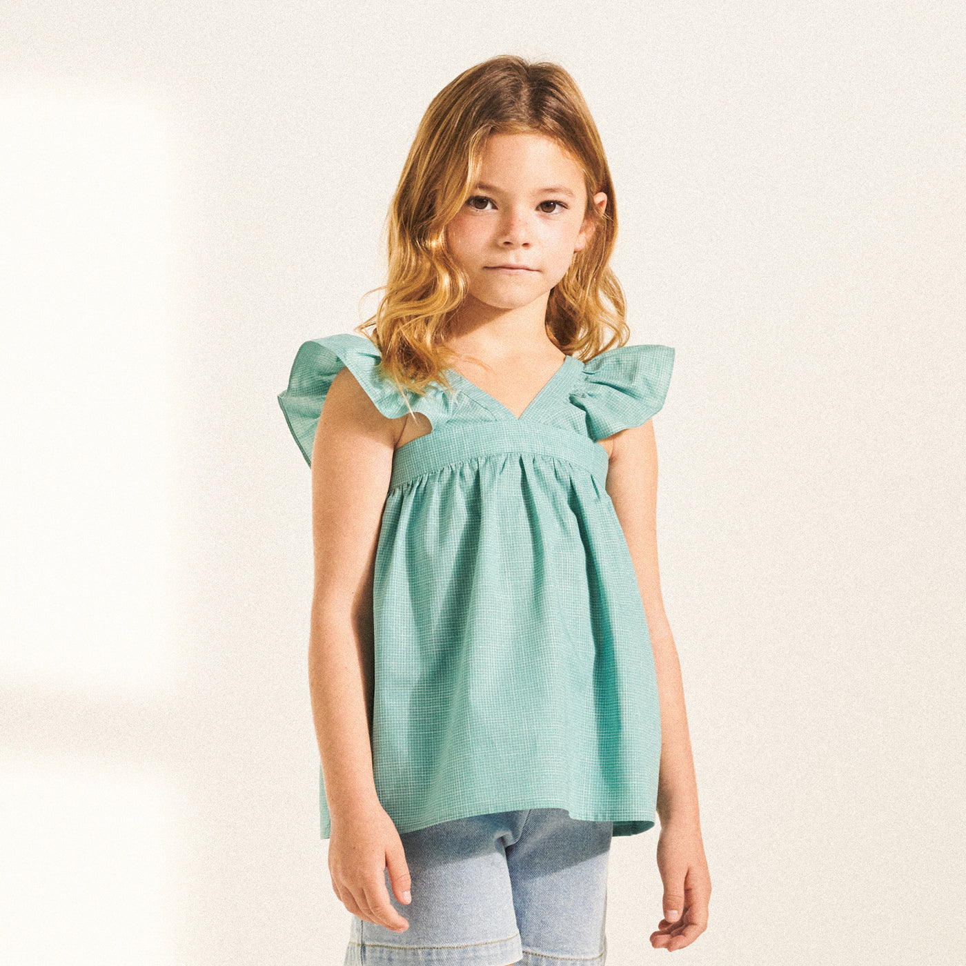 Girl in turquoise blouse with ruffle sleeves from Bonpoint Spring Summer 2022 Collection
