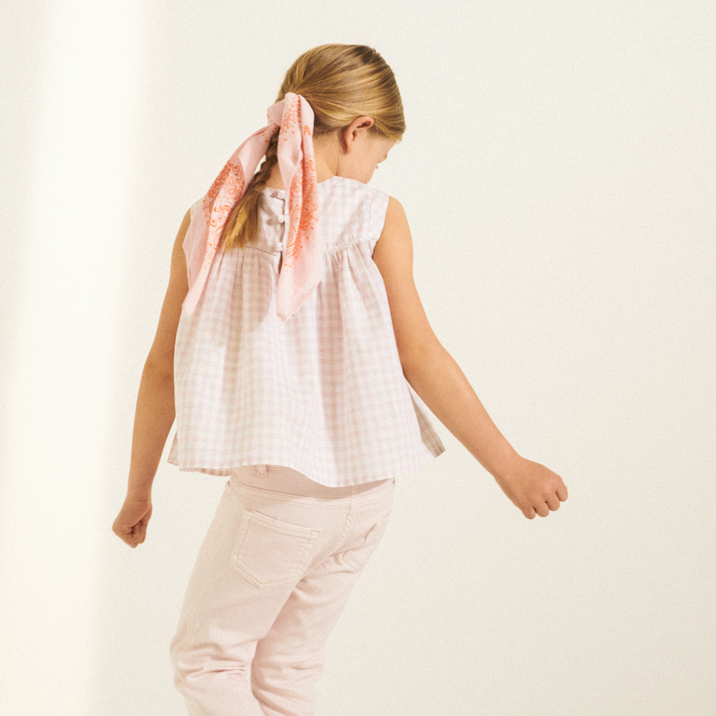 Back of girl in pale pink sleeveless blouse with a pink ribbon in her ponytail from Bonpoint Spring Summer 2022 Collection
