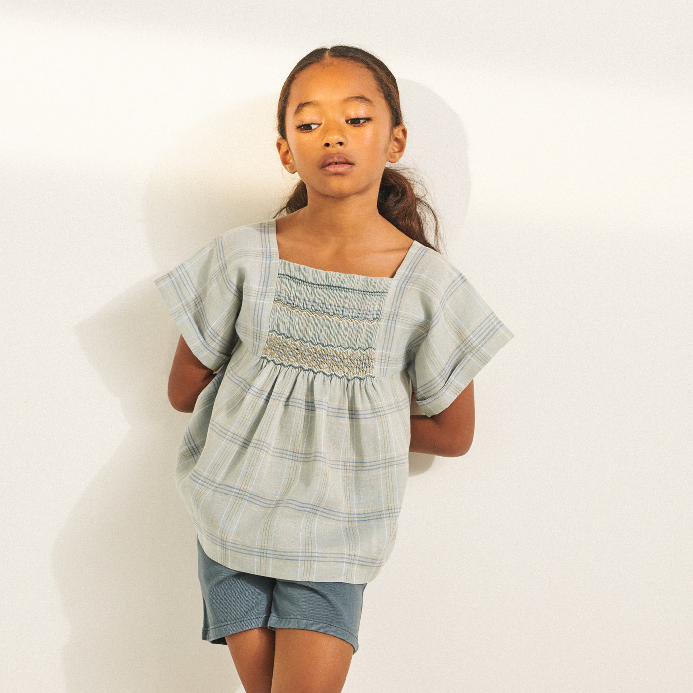 Girl in light grey-blue blouse with embroidery from Bonpoint Spring Summer 2022 Collection