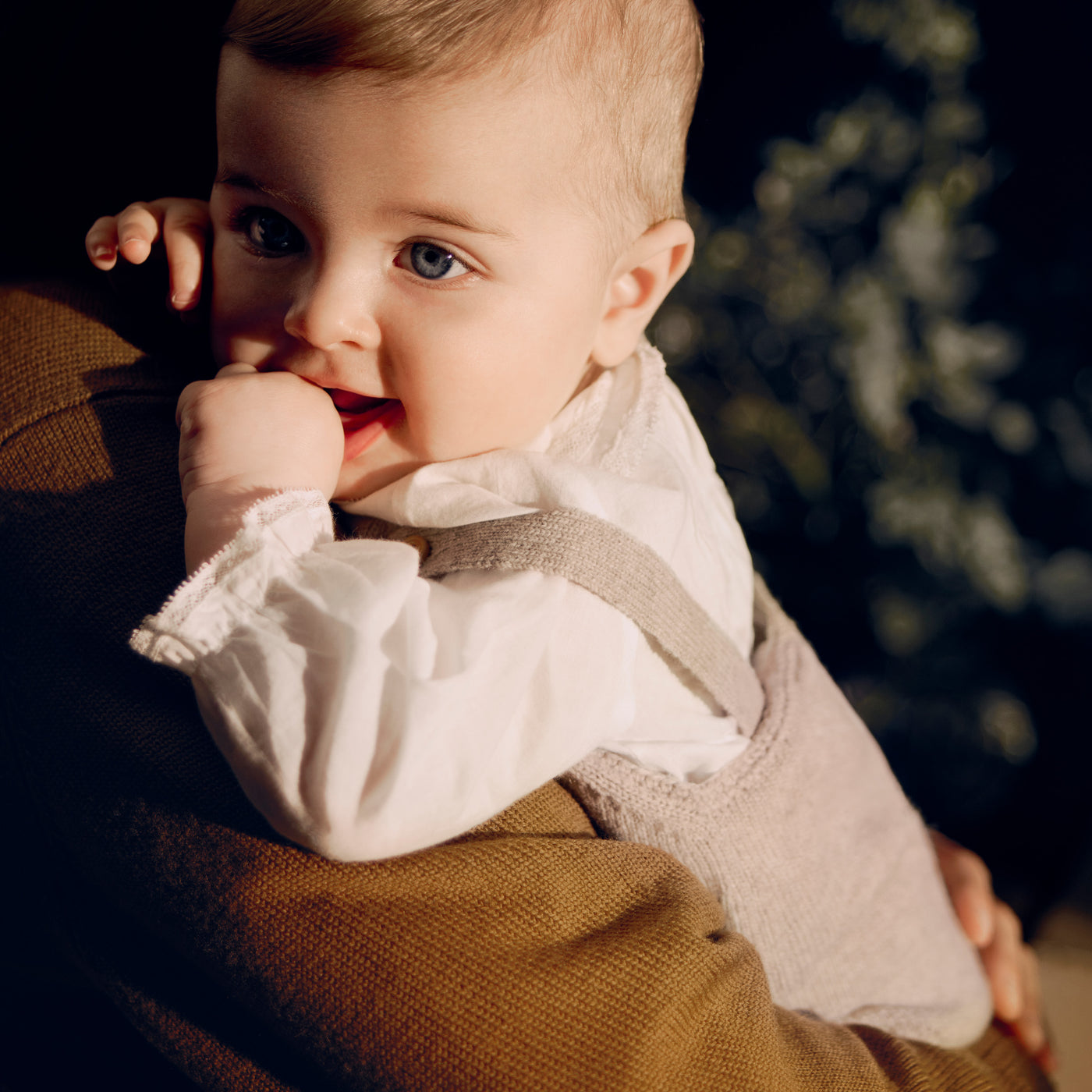 Bonpoint baby being held wearing tan knit overalls with cream collared shirt underneath