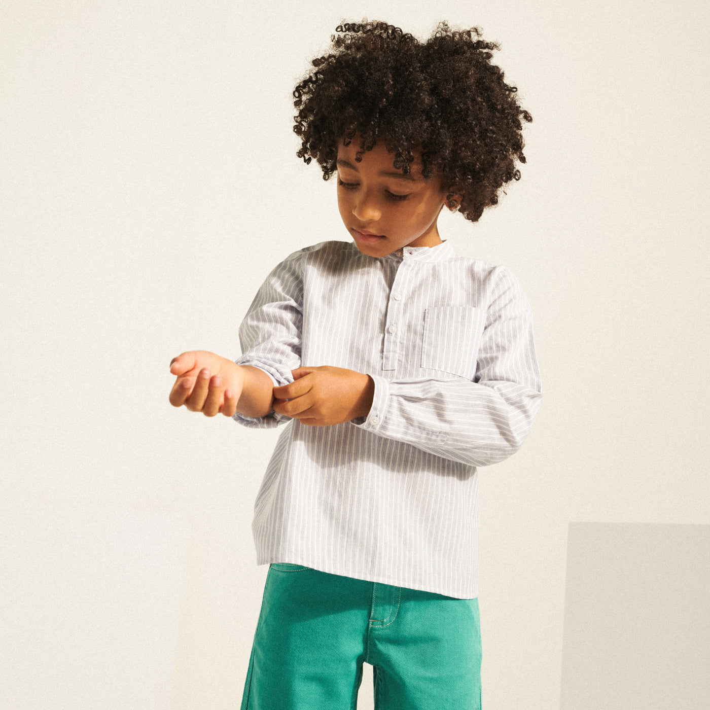 Boy fixing the sleeve of his blue and white stripe shirt from Bonpoint Spring Summer 2022 Collection