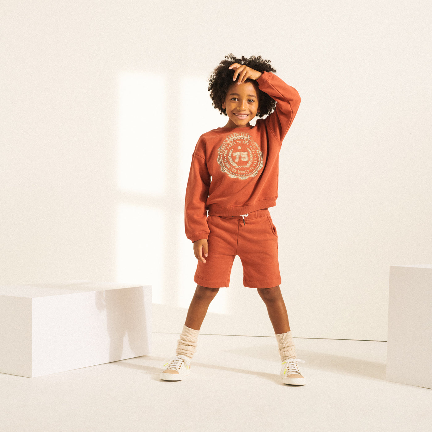 Boy smiling in matching orange sweat set from Bonpoint Spring Summer 2022 Collection