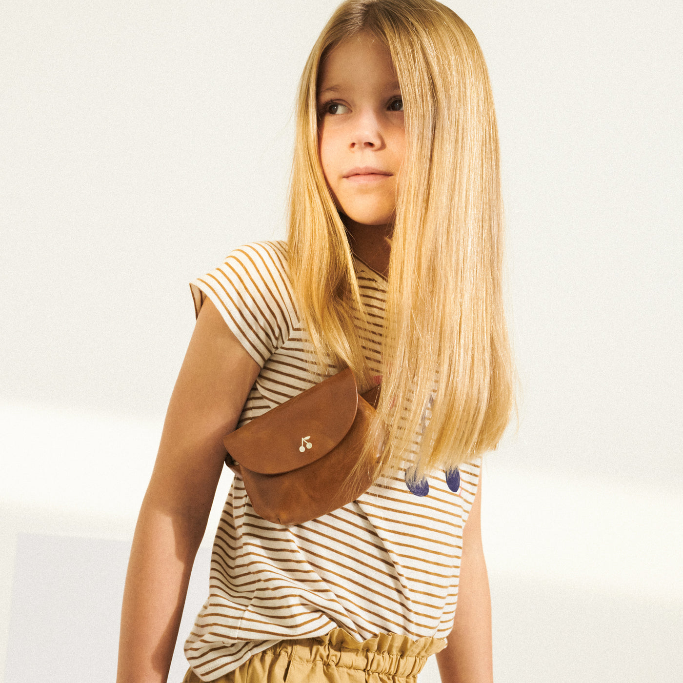 Girl in striped shirt with brown belt bag across chest from Bonpoint Spring Summer 2022 Collection