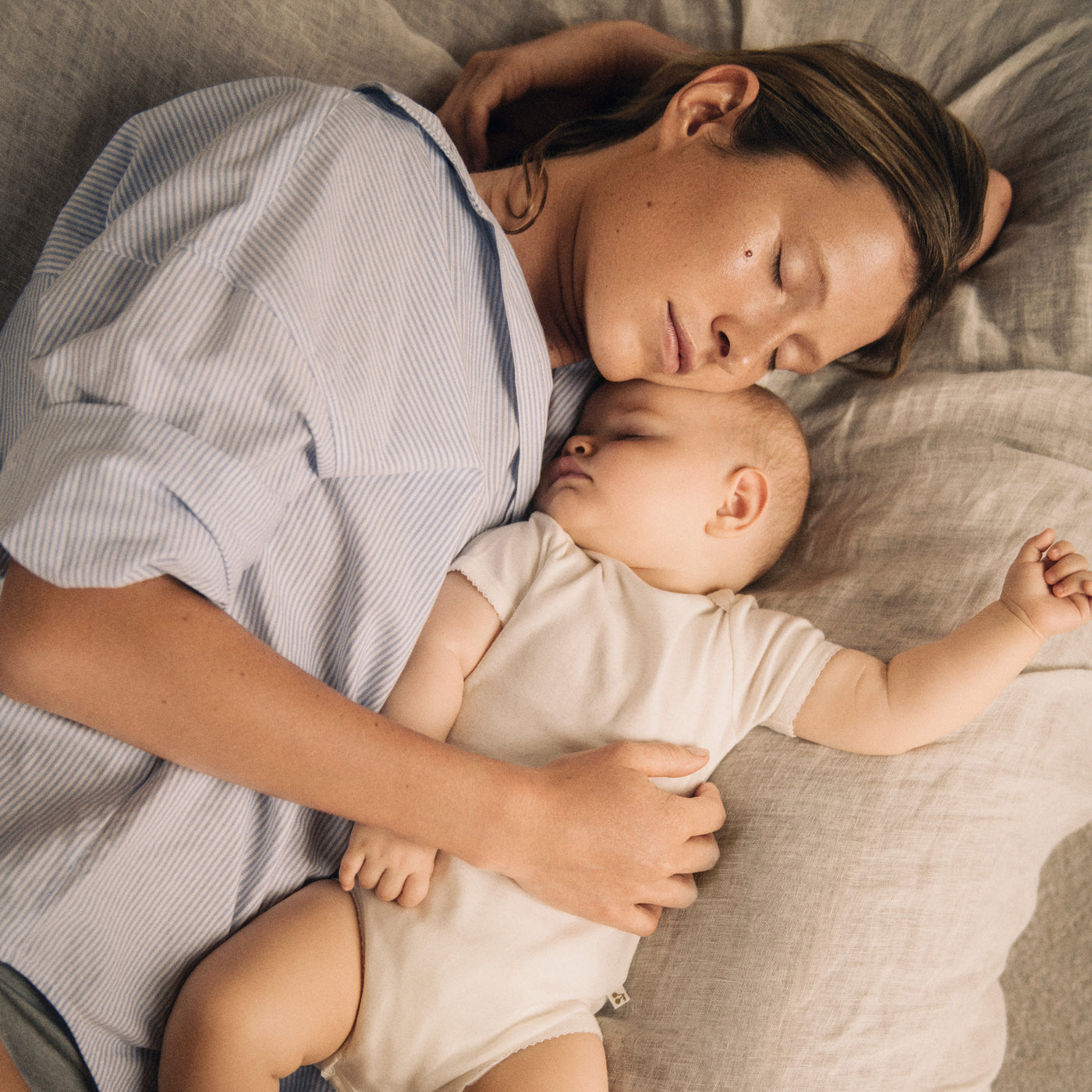 Bonpoint woman and baby sleeping on neutral linen