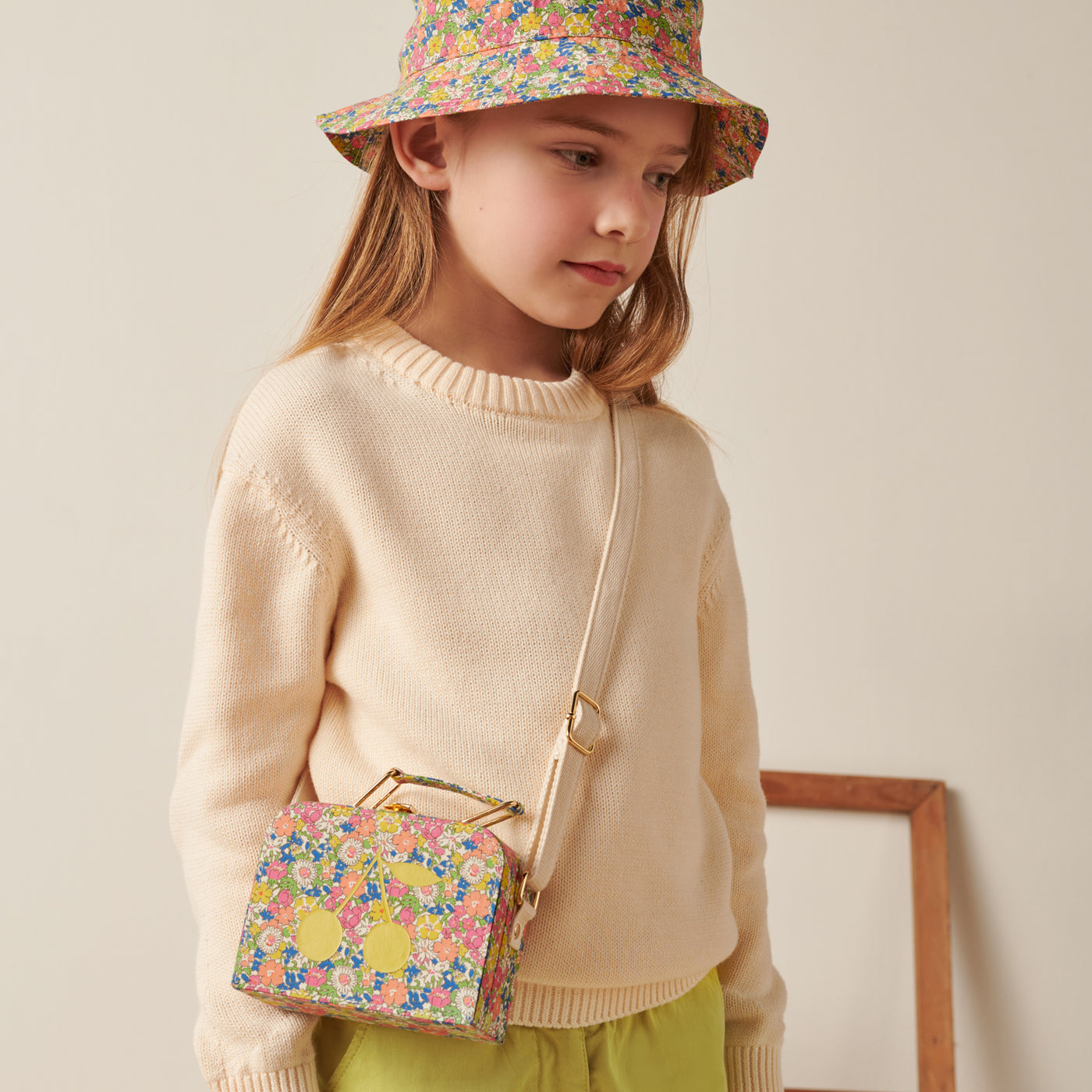 Girl standing in pale sweater with matching crossbody bag and bucket hat from Bonpoint Pre-Fall 2022 Collection