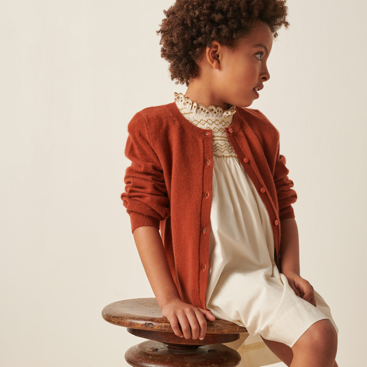 Girl in cream dress with burnt orange cardigan from Bonpoint Pre-Fall 2022 Collection