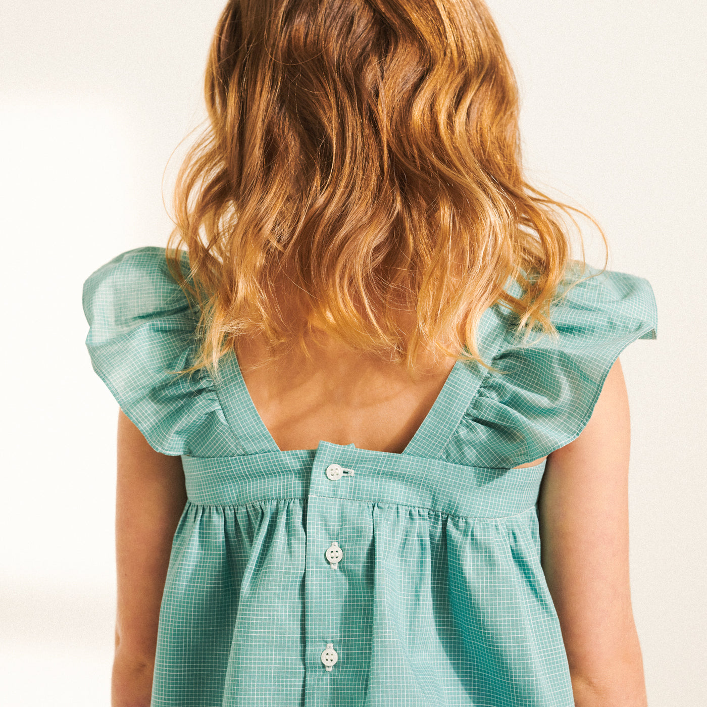 Back of girl in turquoise blouse with ruffle sleeves from Bonpoint Spring Summer 2022 Collection