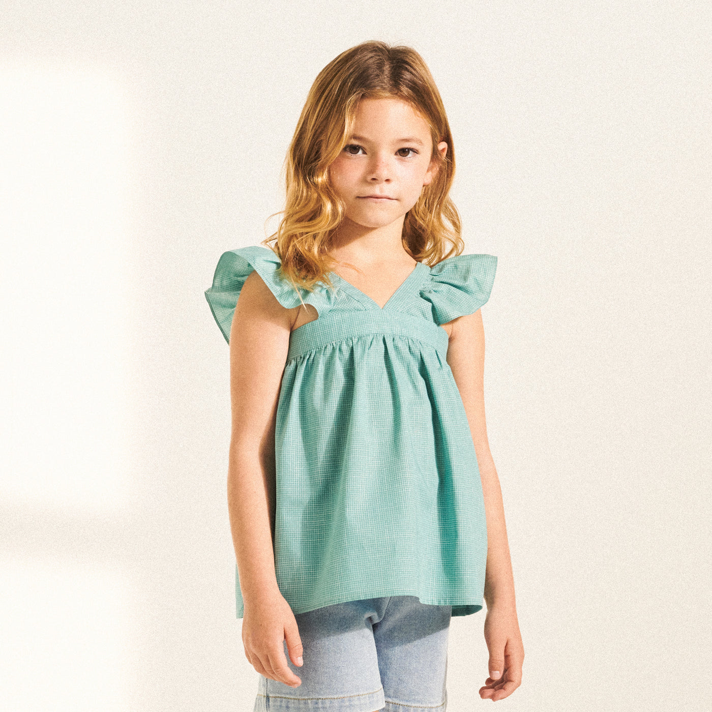 Girl in turquoise blouse with ruffle sleeves from Bonpoint Spring Summer 2022 Collection 