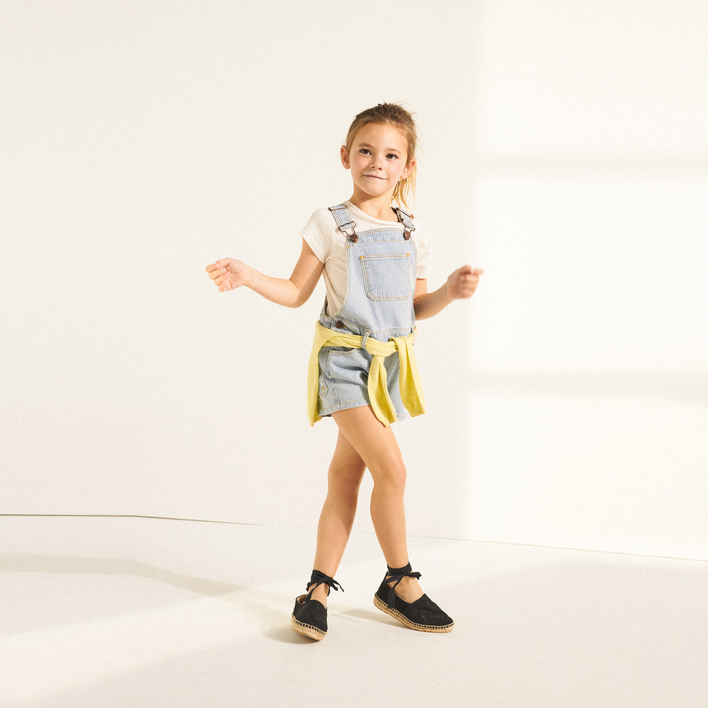 Girl posing in short blue overalls from Bonpoint Spring Summer 2022 Collection