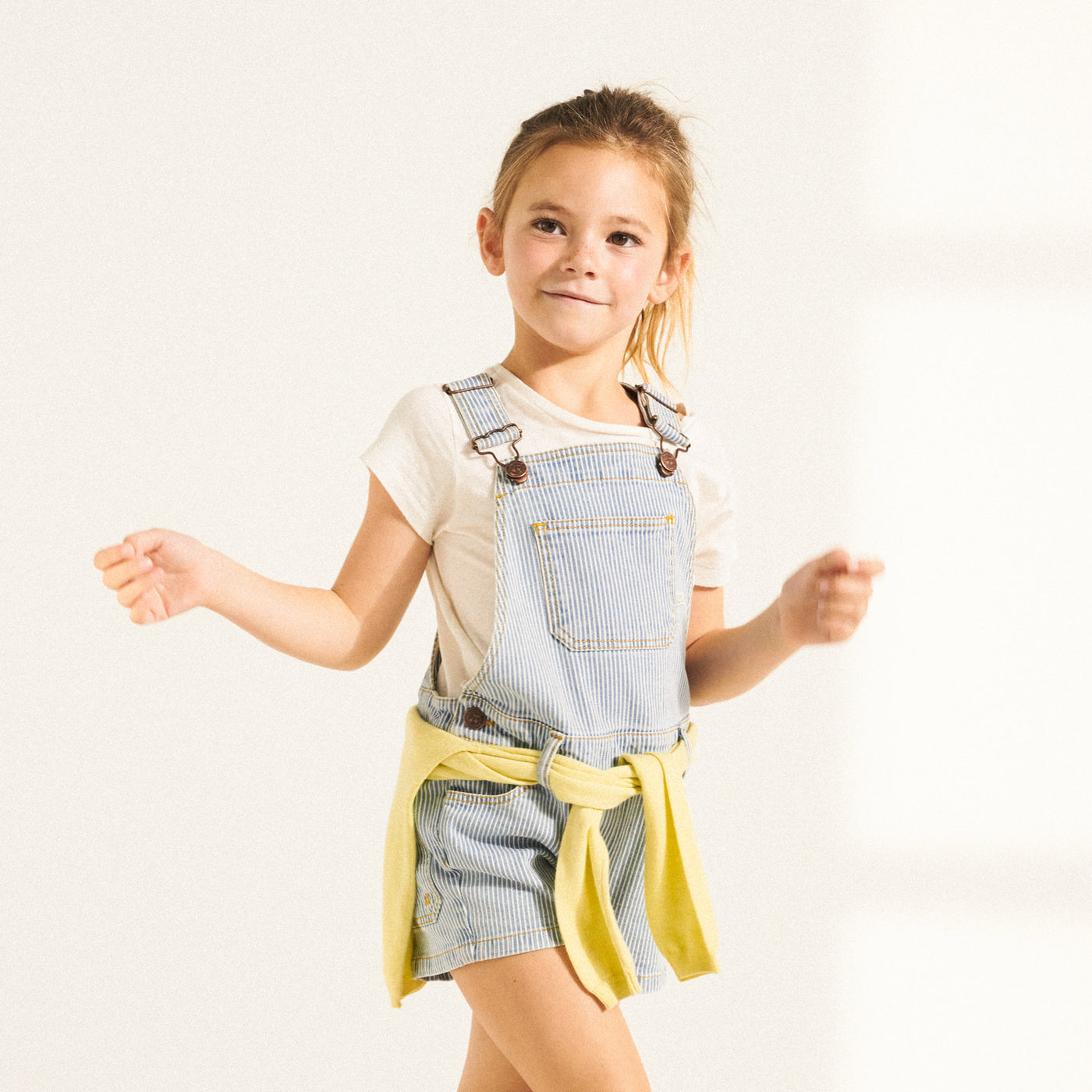 Girl in short blue overalls from Bonpoint Spring Summer 2022 Collection