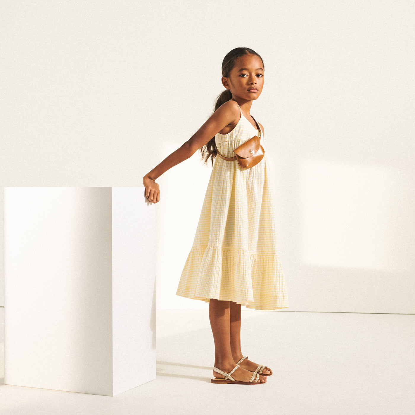 Girl in cream sundress with leather belt bag across chest from Bonpoint Spring Summer 2022 Collection