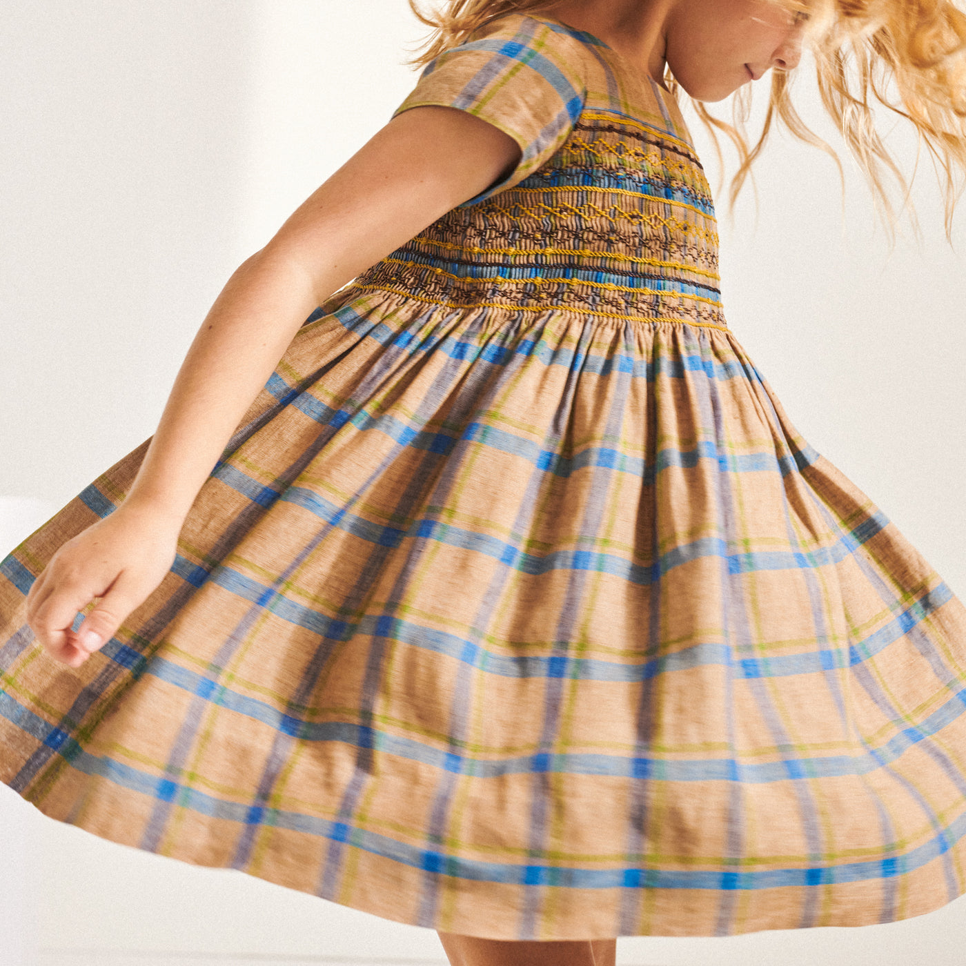 Girl twirling in orange and blue plaid dress from Bonpoint Spring Summer 2022 Collection