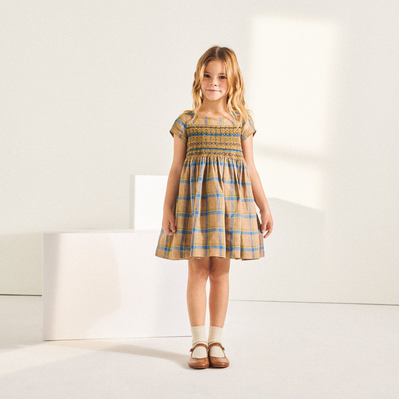 Girl standing in orange and blue plaid dress from Bonpoint Spring Summer 2022 Collection