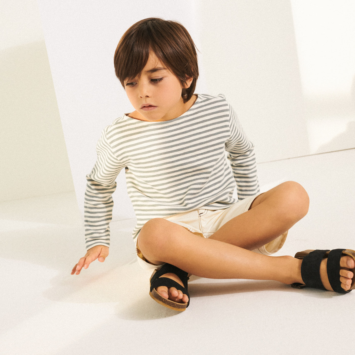 Boy sitting in long sleeve grey and white shirt from Bonpoint Spring Summer 2022 Collection