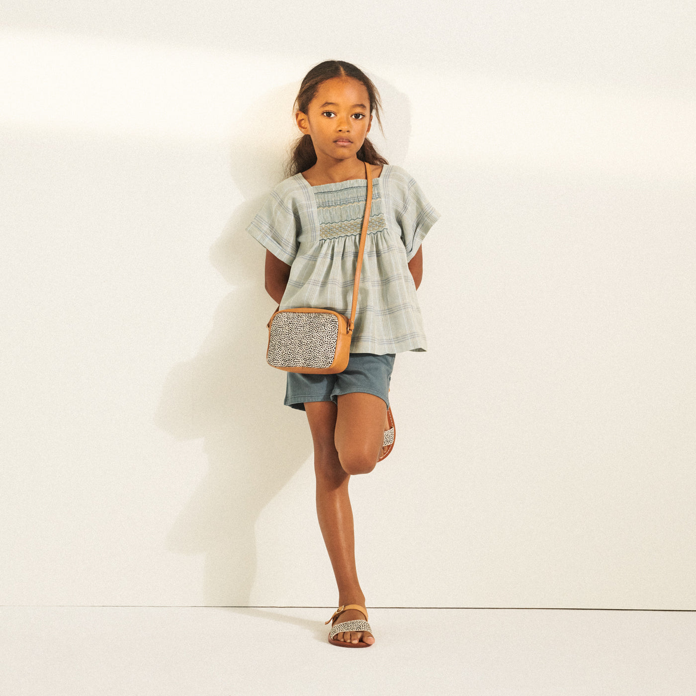 Girl posing in light grey-blue blouse with Bonpoint crossbody bag from Bonpoint Spring Summer 2022 Collection