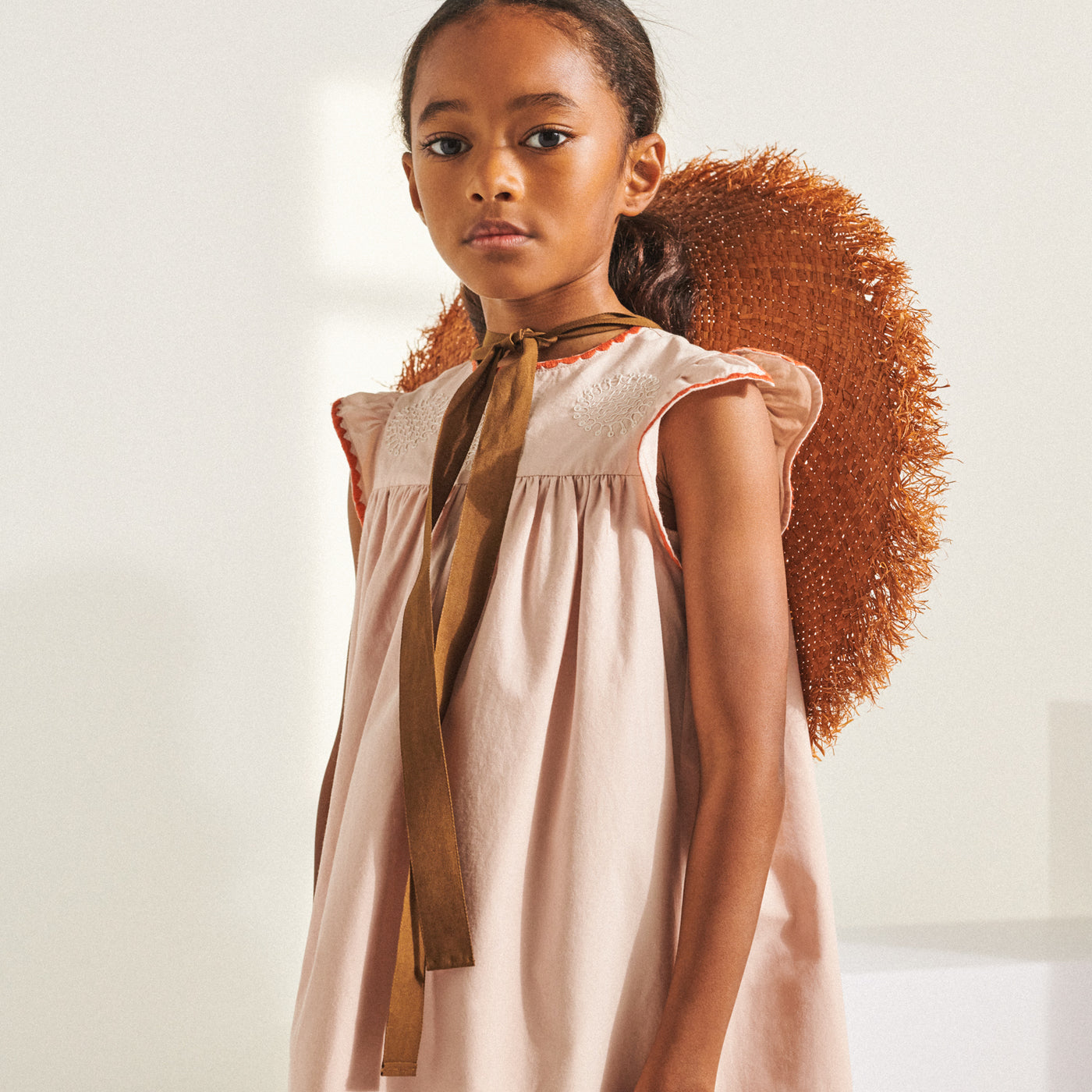 Girl in pale pink dress with mauve straw hat from Bonpoint Spring Summer 2022 Collection