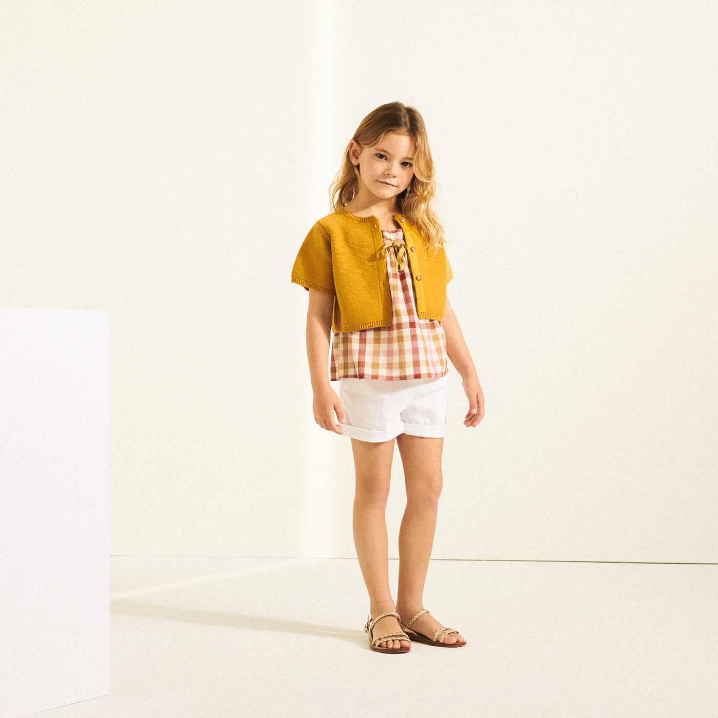 Girl in pink and yellow checkered shirt with a yellow cardigan from Bonpoint Spring Summer 2022 Collection