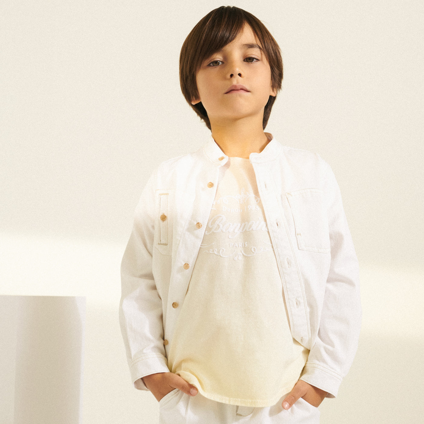 Boy in cream Bonpoint shirt with white denim jacket from Bonpoint Spring Summer 2022 Collection