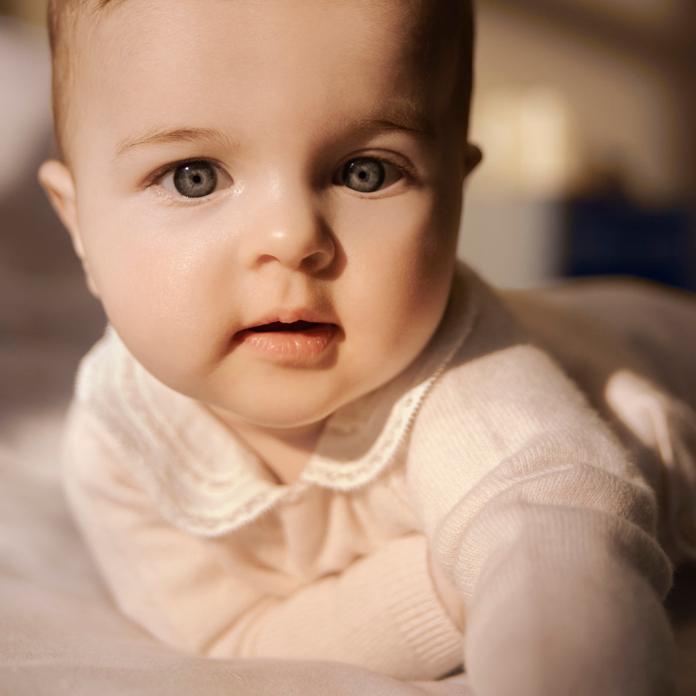 Bonpoint baby with light eyes wearing pale pink sweater with detailed white collar